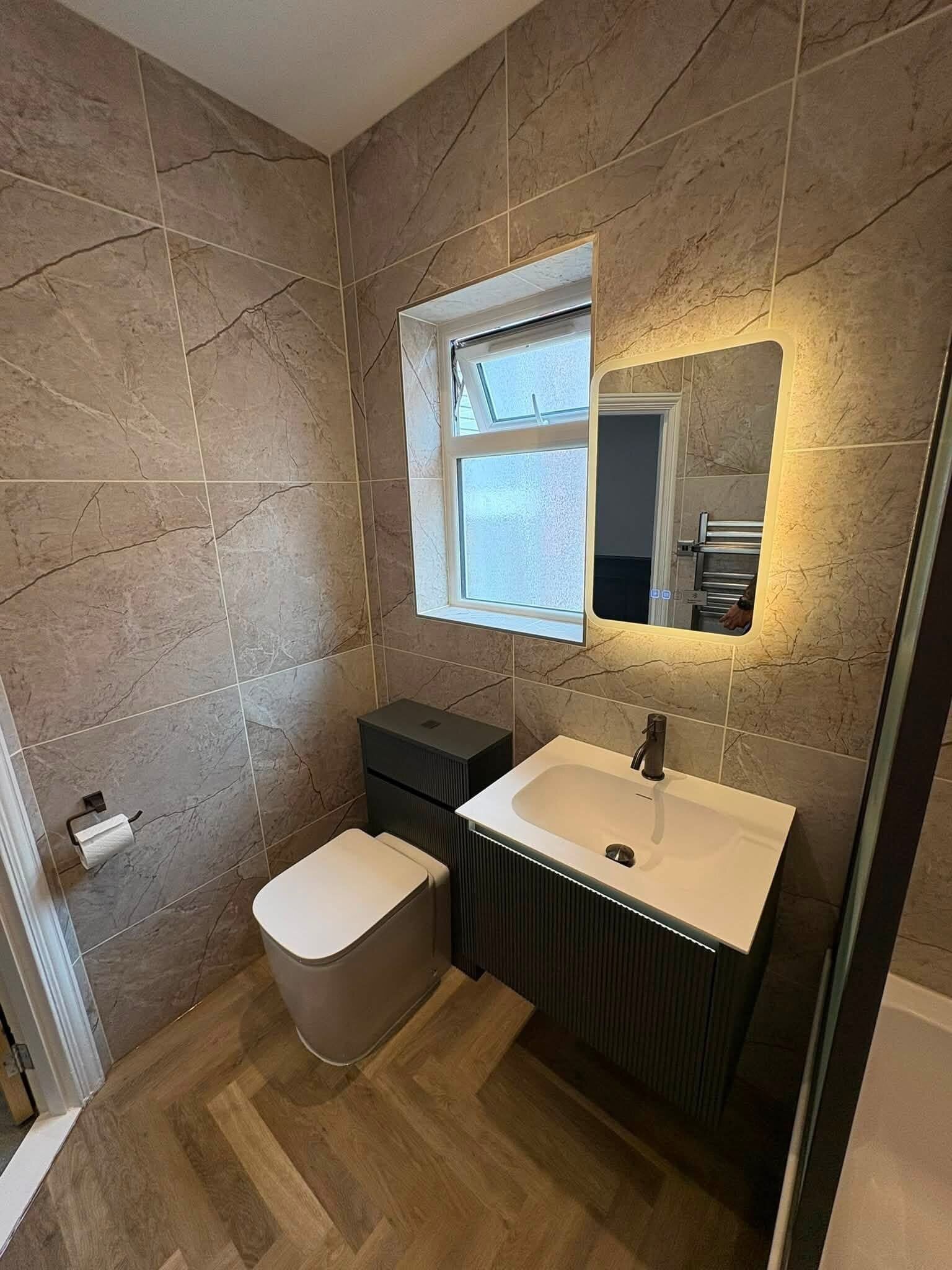 Customer bathroom transformation in Portsmouth featuring wood-effect flooring, wall-hung furniture and illuminated mirror.