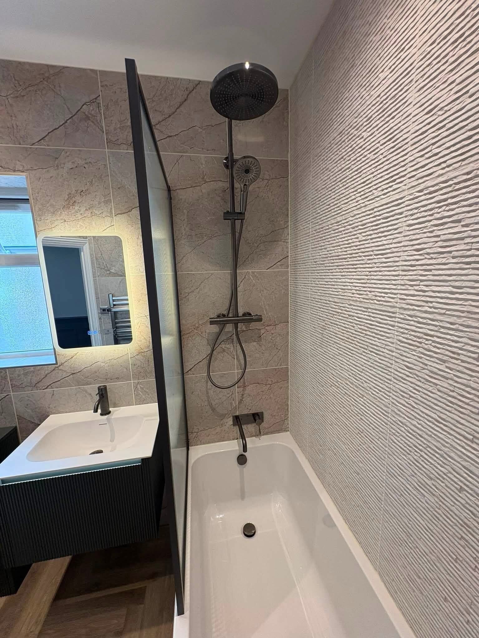 Portsmouth customer bathroom featuring textured wall tiles, black shower fittings and a contemporary vanity unit.