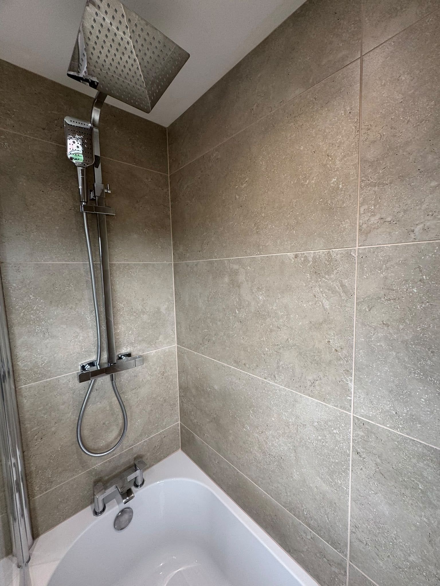 Chrome shower fitting and glass enclosure against large neutral stone-effect wall tiles.
