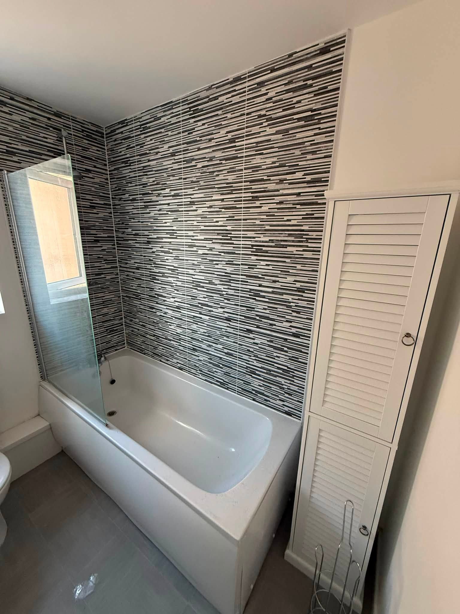 Before photo of the original bathroom with a fitted bath, patterned wall tiles and traditional radiator.