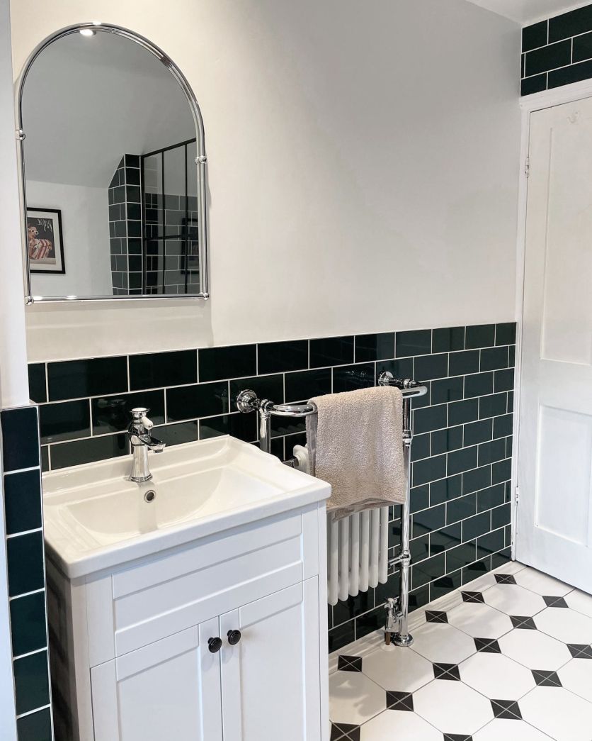 A traditional-style white shaker vanity unit with a ceramic basin and chrome taps, set against a half-wall of glossy dark green metro tiles.