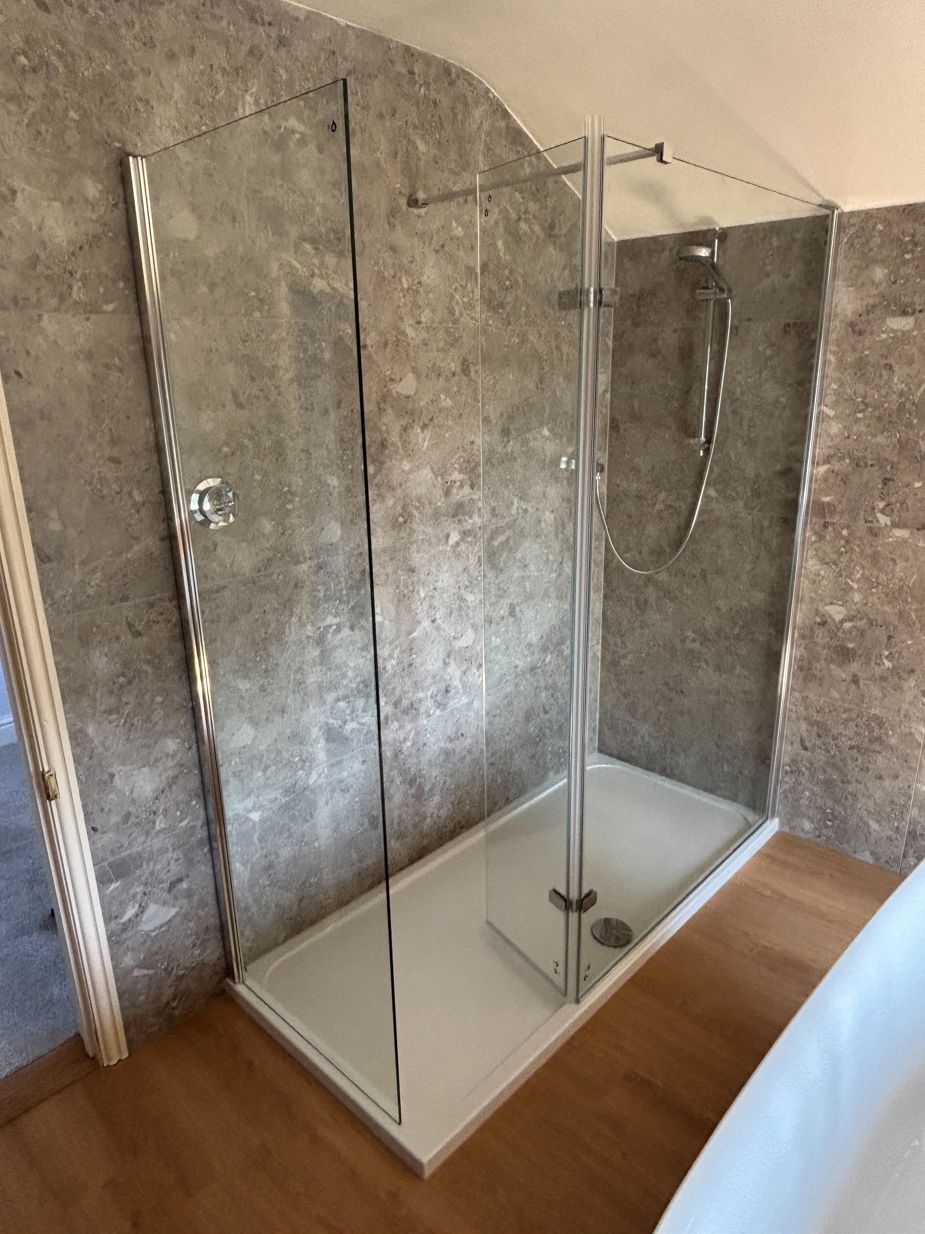 Walk-in shower enclosure with chrome fittings and neutral stone-effect wall tiles.