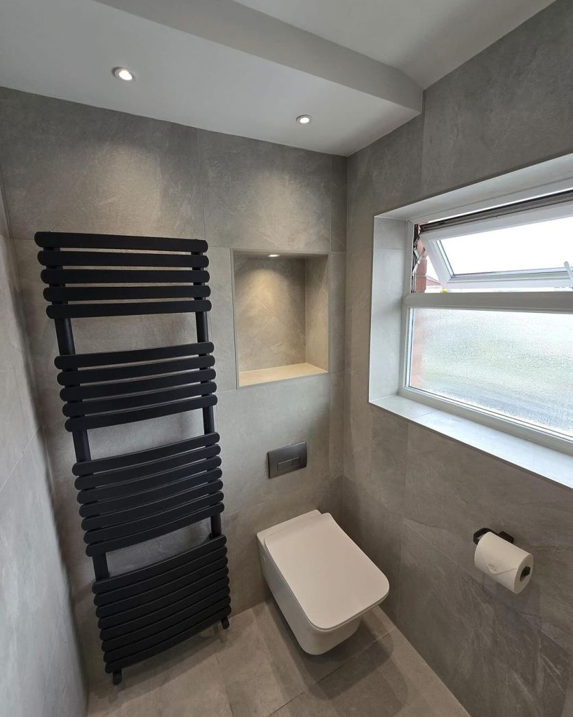 An Elbert wall hung toilet and Eventon anthracite towel rail set against grey stone effect tiles in a modern bathroom.