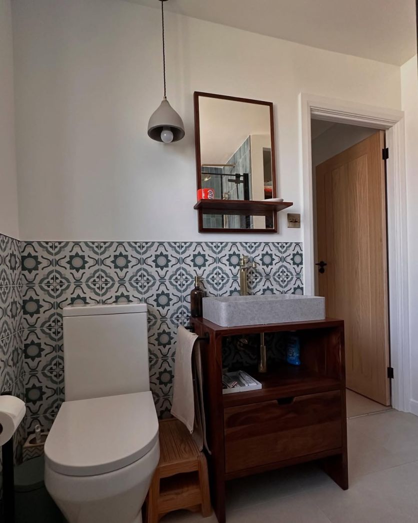 A mid-century modern cloakroom featuring a dark wood vanity with a grey stone countertop basin, a Downton brushed gold tall tap, and decorative geometric patterned wall tiles.