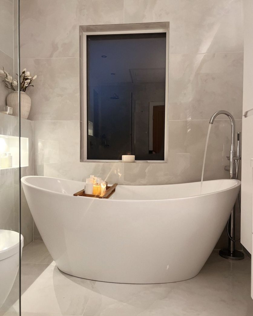 A luxury spa-style bathroom featuring a Lambi freestanding white acrylic bath and a Twyford chrome floor-standing mixer, surrounded by Osaka White super polished onyx-effect porcelain tiles.
