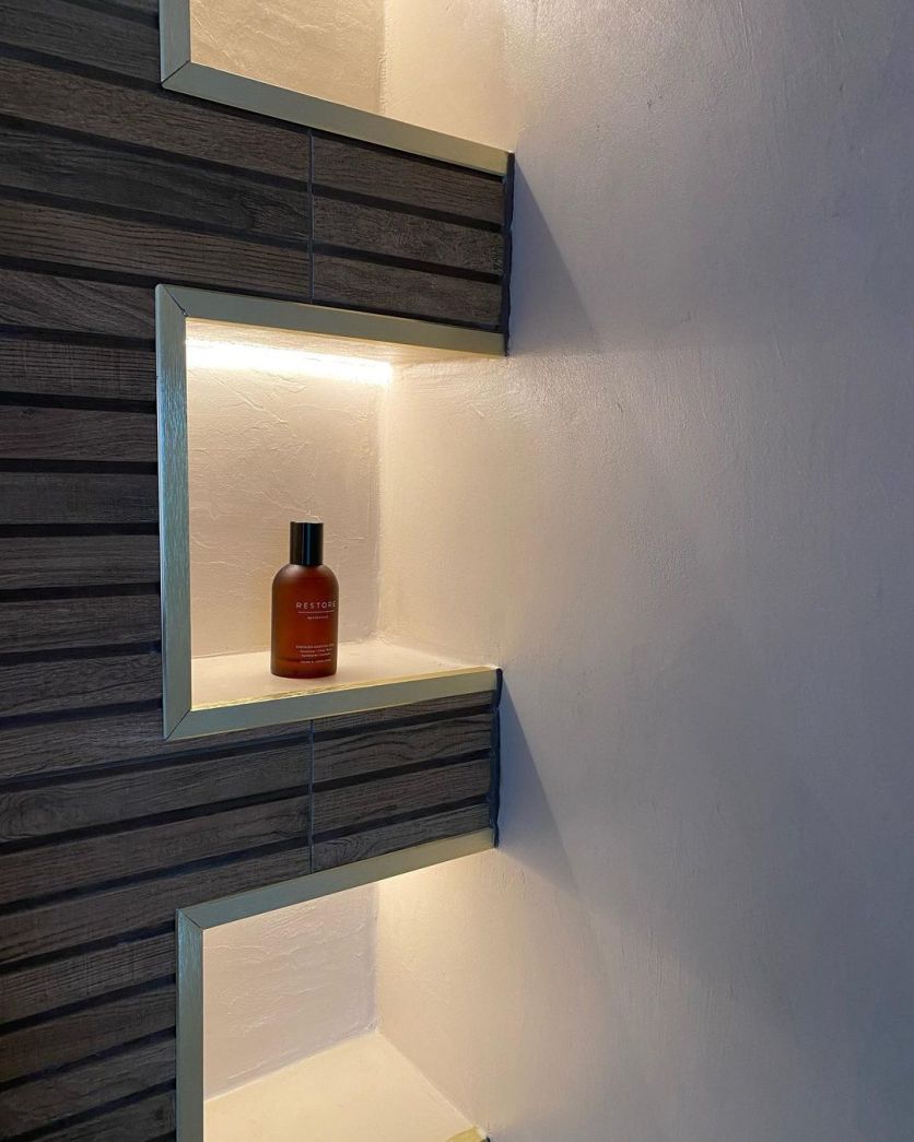 Madera Decor slatted wood tiles framed with gold square trim in an illuminated recessed bathroom niche.