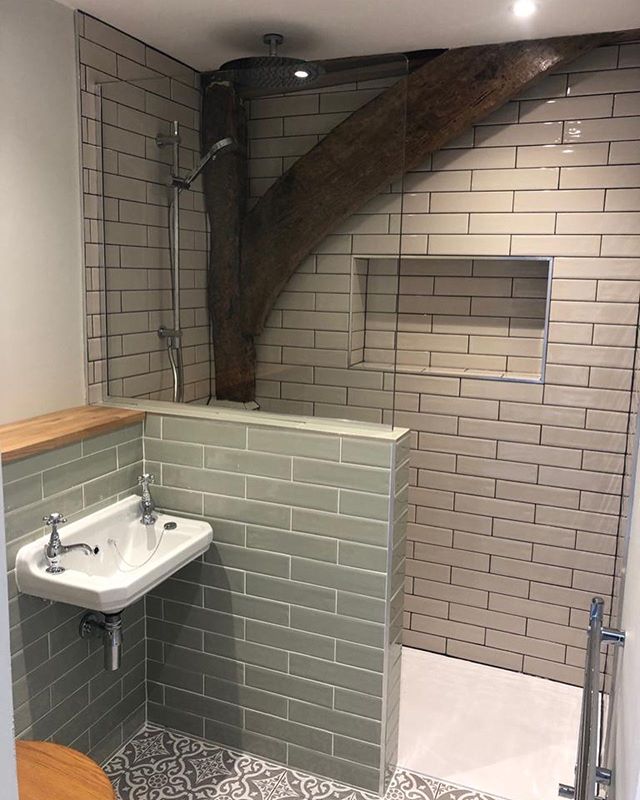 A rustic-industrial walk-in shower featuring a natural reclaimed timber beam integrated into soft cream and sage green metro tiling, paired with a traditional wall-hung cloakroom basin and chrome crosshead taps.