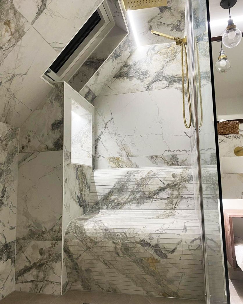 A luxury walk-in shower featuring large-format marble effect wall tiles and a unique curved tiled seating bench with a fluted texture.