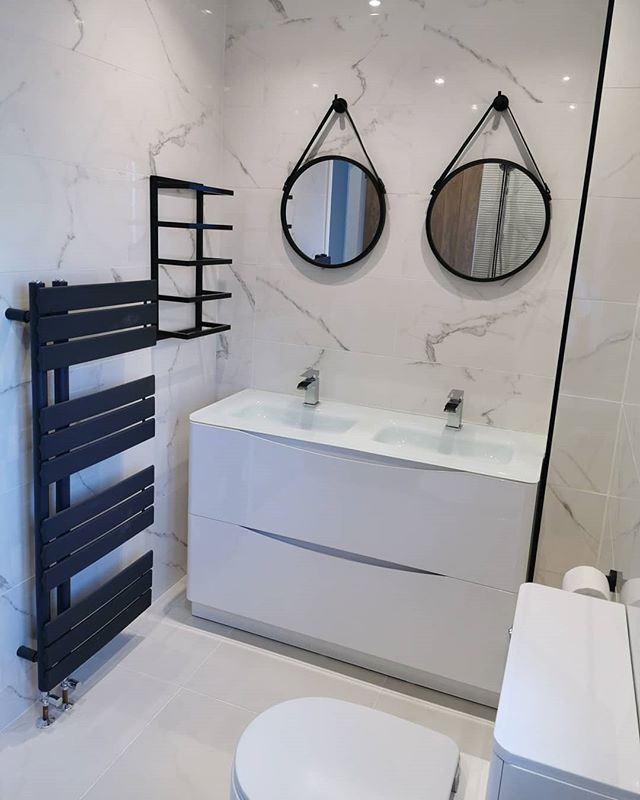 A modern double white gloss vanity unit with twin basins and chrome taps, paired with round black hanging mirrors against marble effect tiling.
