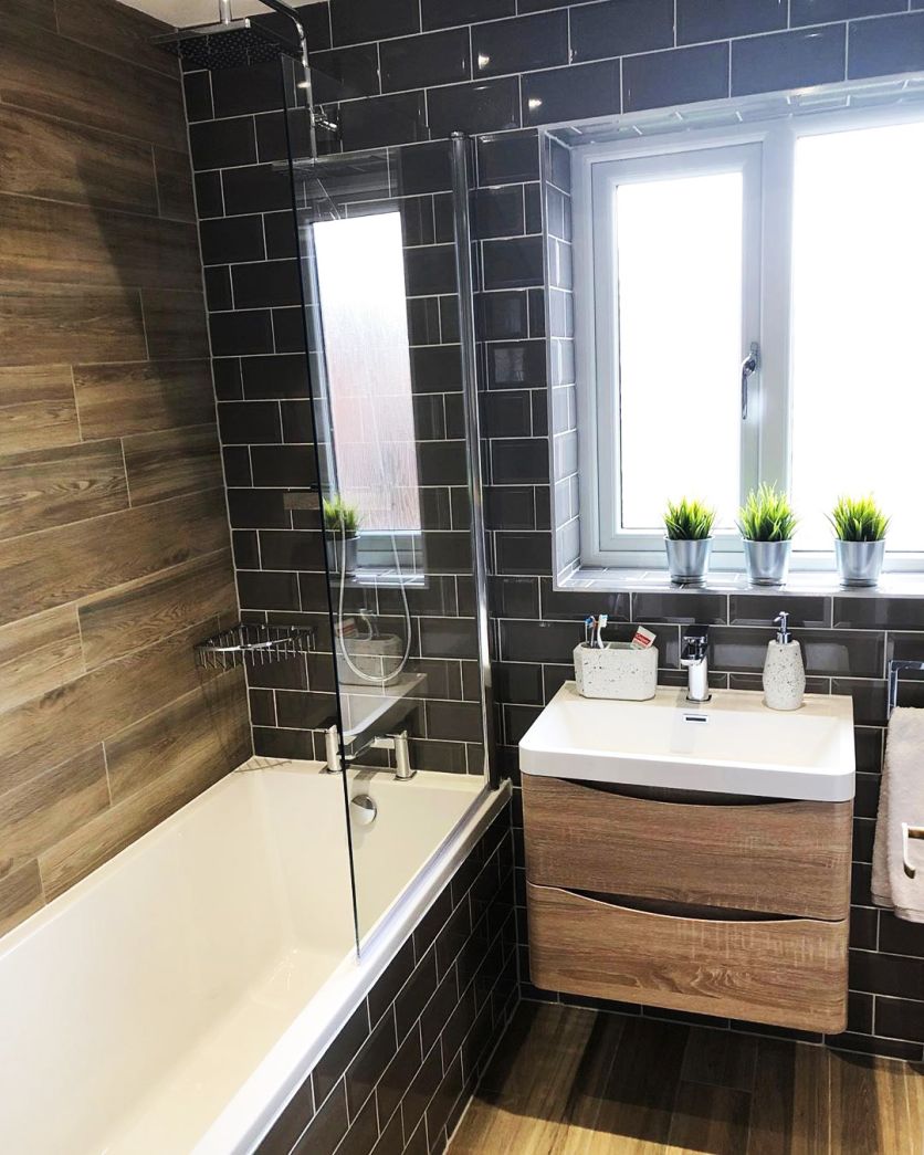 A modern bathroom featuring dark grey gloss metro tiles contrasted against warm wood-effect plank walling and a floating light oak vanity unit with a white ceramic basin.