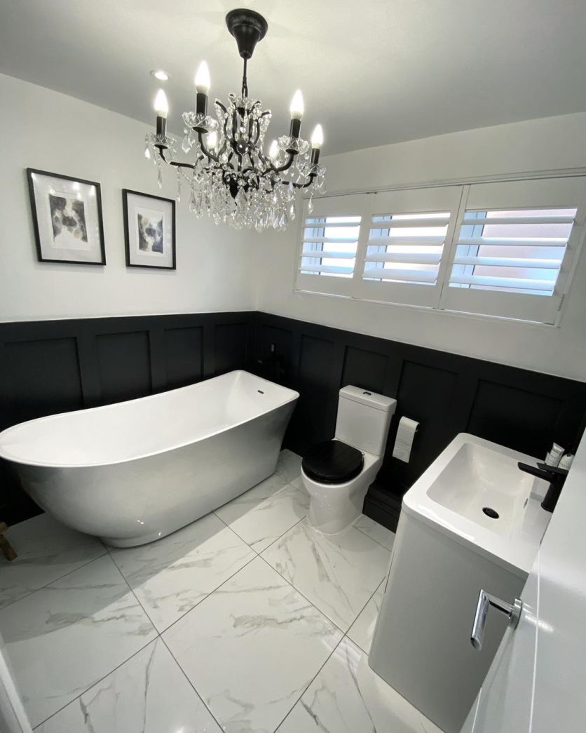 A luxurious monochrome bathroom featuring a white freestanding slipper bath set against bold black wood wall panelling and elegant white marble-effect floor tiles.