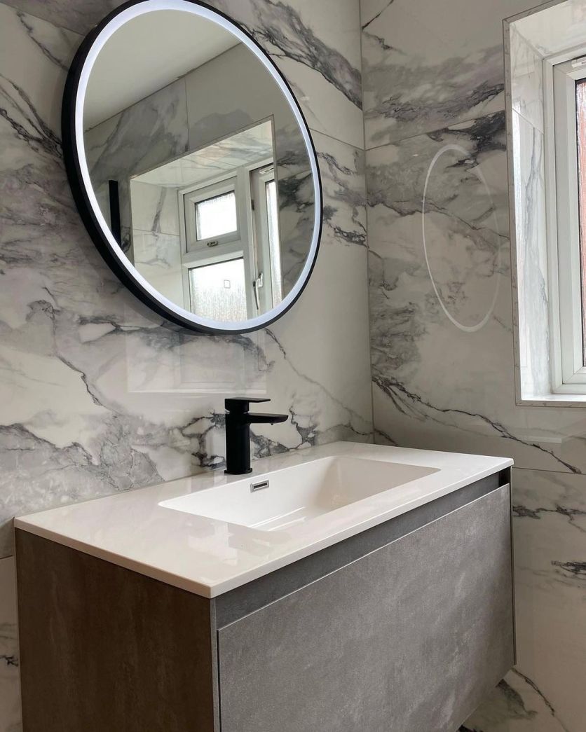 Modern bathroom with marble-effect walls, a grey wall-hung vanity, black mixer tap and round LED mirror.