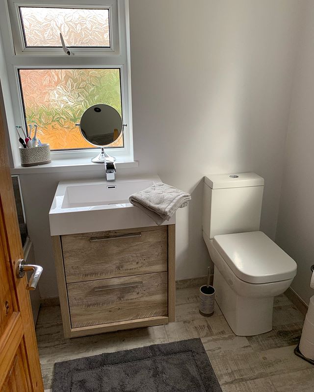 A light oak wood-effect vanity unit with a white square inset basin and chrome tap, situated next to a modern white close-coupled toilet.