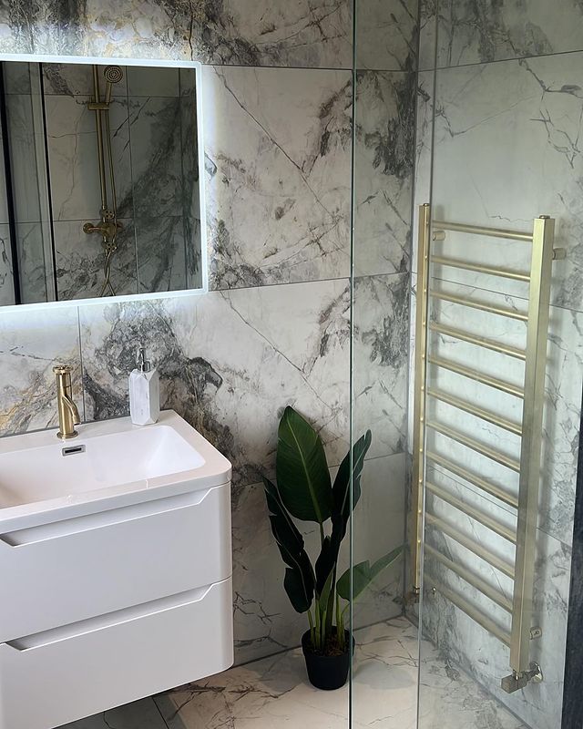 Modern marble bathroom with brushed gold fixtures, white wall-hung vanity and an illuminated mirror.
