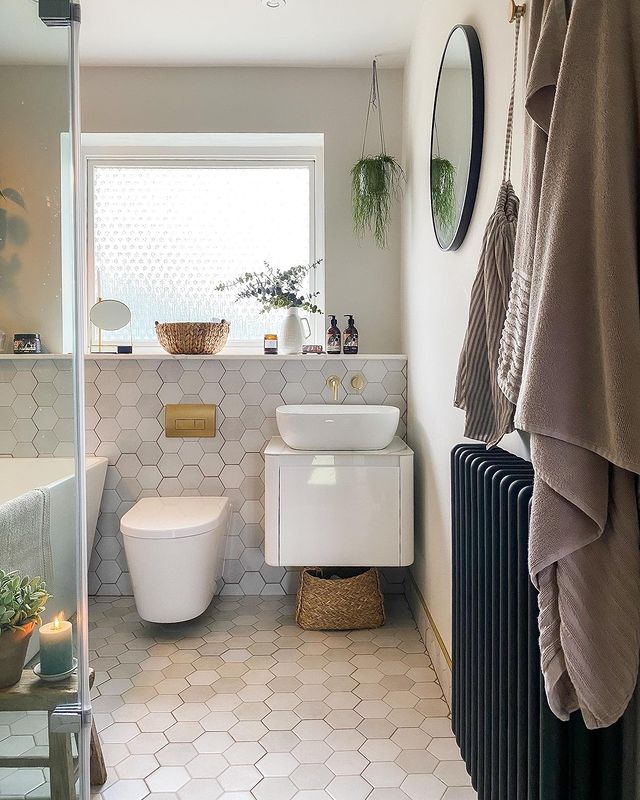 Modern neutral bathroom with hexagon wall and floor tiles, wall-hung vanity, round basin, gold accents and column radiator.