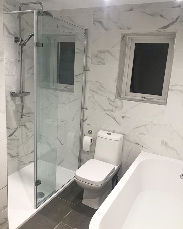 A modern white close-coupled toilet positioned between a glass walk-in shower featuring a chrome rainfall head and a white inset bathtub.