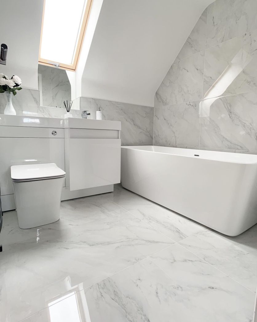 Modern white bathroom with marble-effect floor and wall tiles, freestanding bath and white gloss combination vanity basin and WC unit.