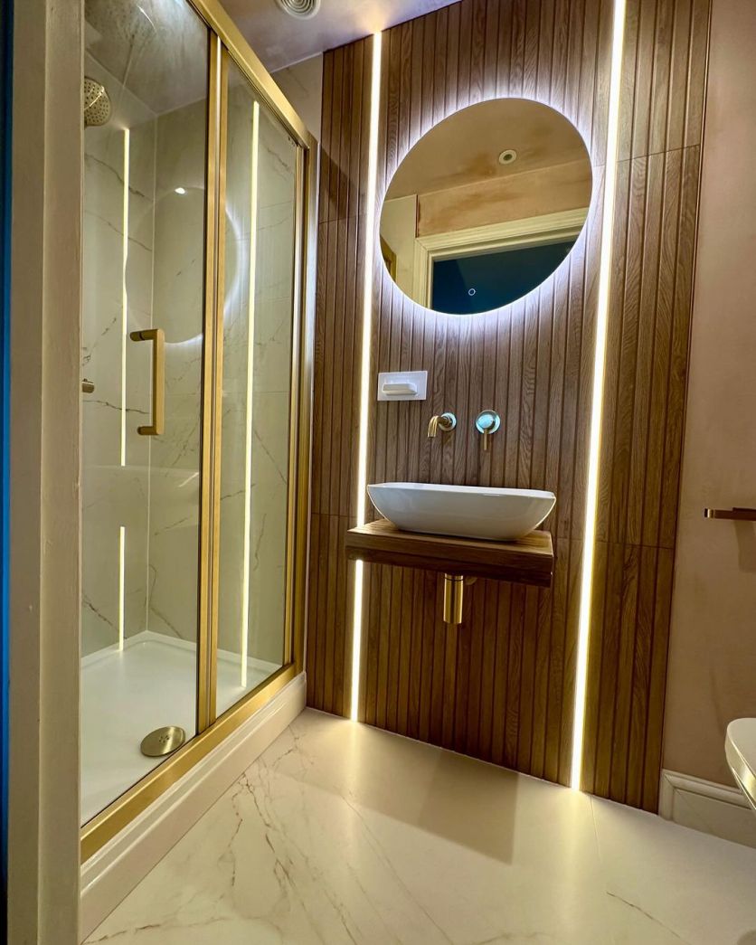 Dune 4D wood paneling with vertical LED strips frames a Felix mirror, Elora gold tap, and Fabio shower door.