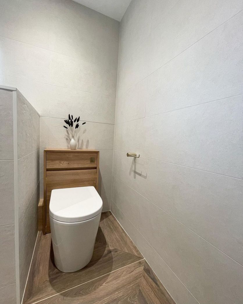 A minimalist cloakroom featuring a Snowdon natural oak WC unit with a Froxfield back-to-wall toilet, Moray champagne gold toilet roll holder, and Cello Nogal wood-effect porcelain flooring.