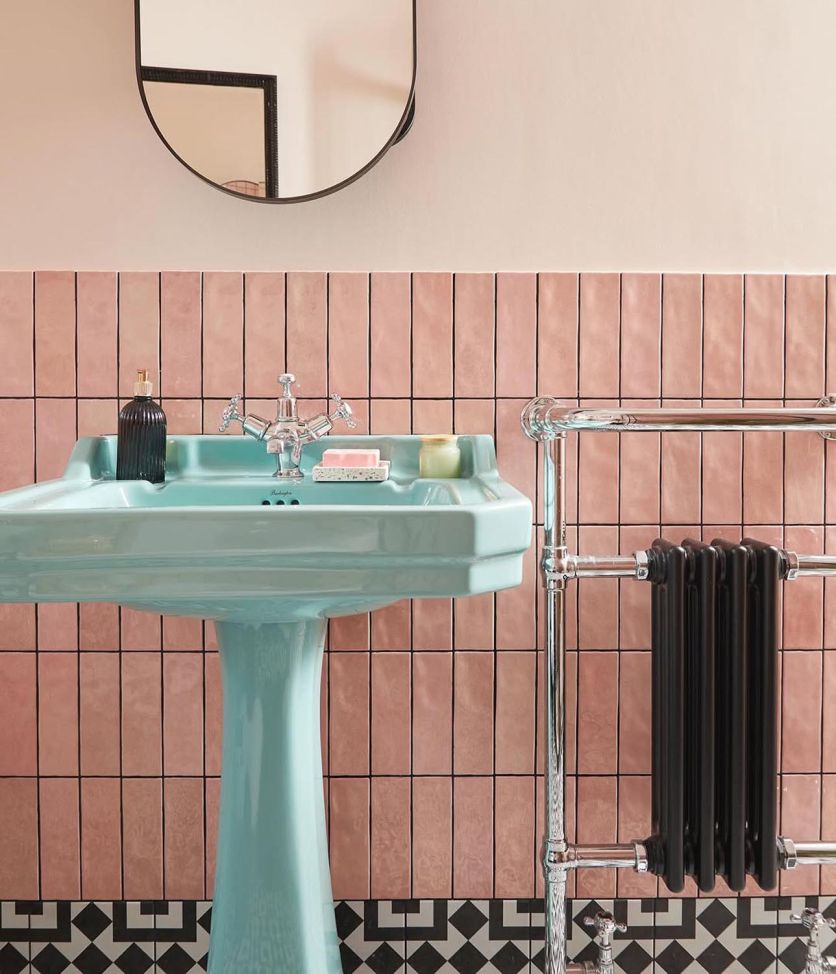 A vibrant retro-inspired bathroom featuring a pastel blue pedestal basin, Napoli Rosa pink gloss brick tiles laid vertically, and Cascais Mix patterned monochrome floor tiles.