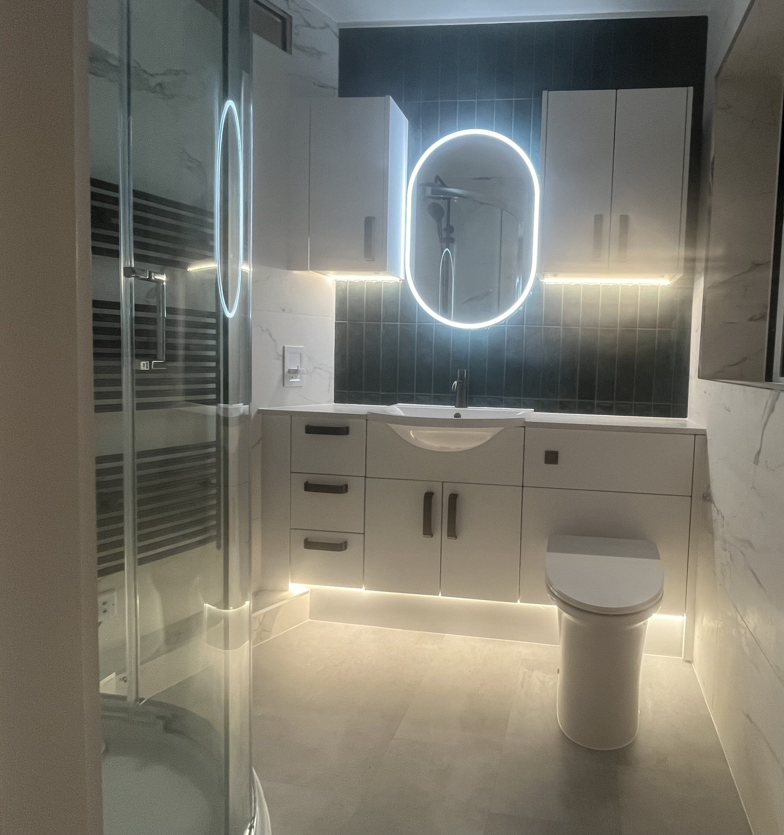 Completed customer bathroom supplied by Easy Bathrooms Chichester with illuminated mirror, dark green tiles and white gloss furniture.