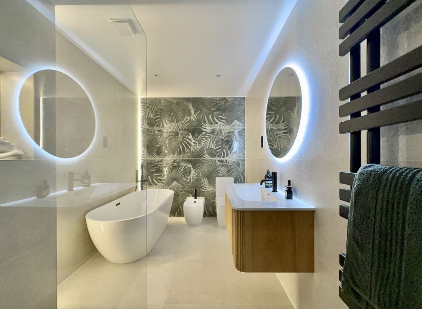 A luxury spa-style bathroom featuring a Wish ribbed natural oak vanity, Felix round backlit LED mirror, and a stunning Bonito Jungle leaf-print porcelain feature wall.
