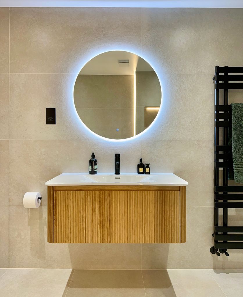A modern bathroom vanity set featuring a Wish ribbed natural oak wall-hung unit, an Elora matt black basin tap, and a Felix round backlit LED mirror against Gandi Concrete Arena porcelain tiles.