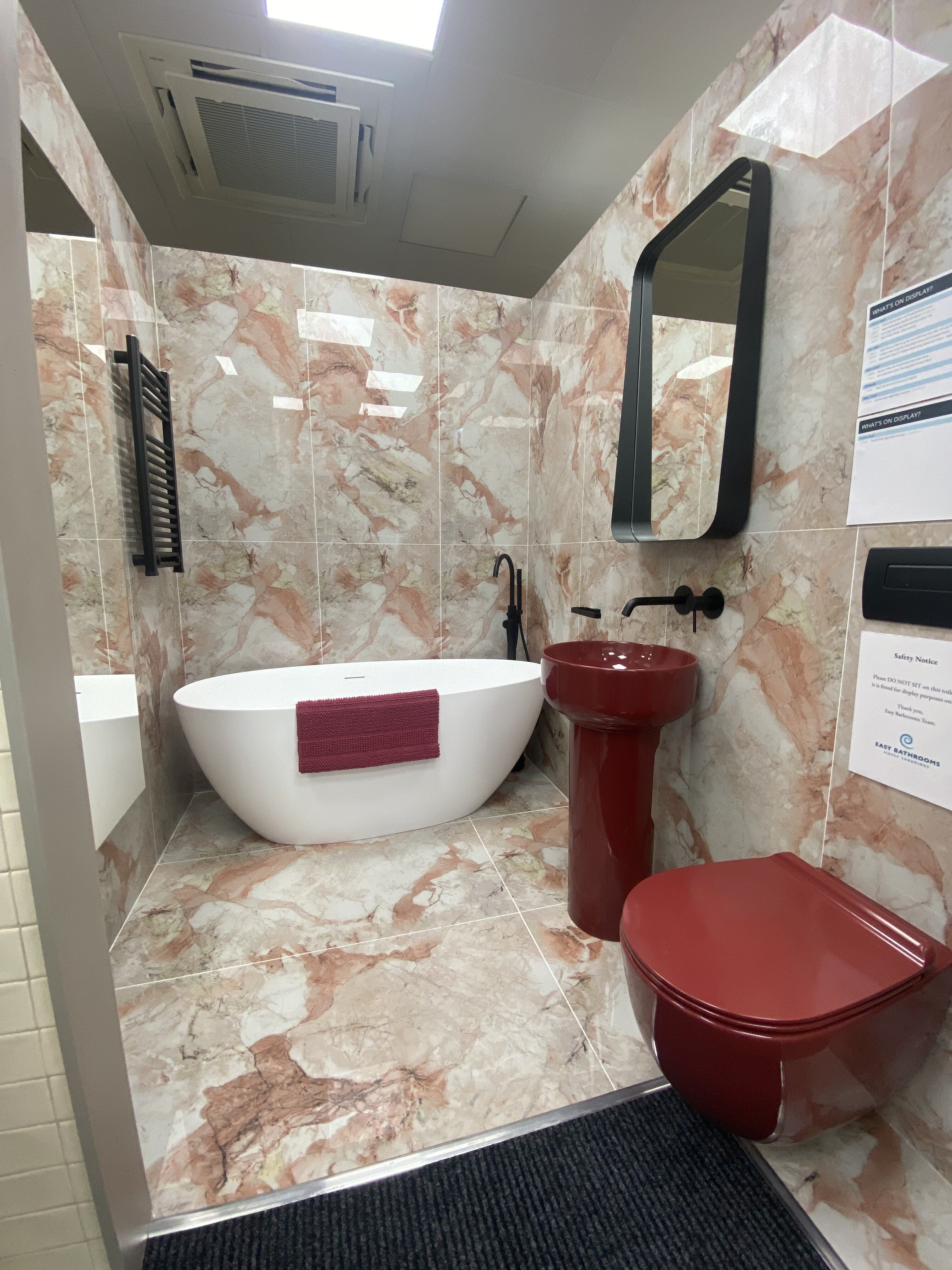 Bold Newbury bathroom display with pink marble-effect tiles, red basin furniture and coordinating accessories.