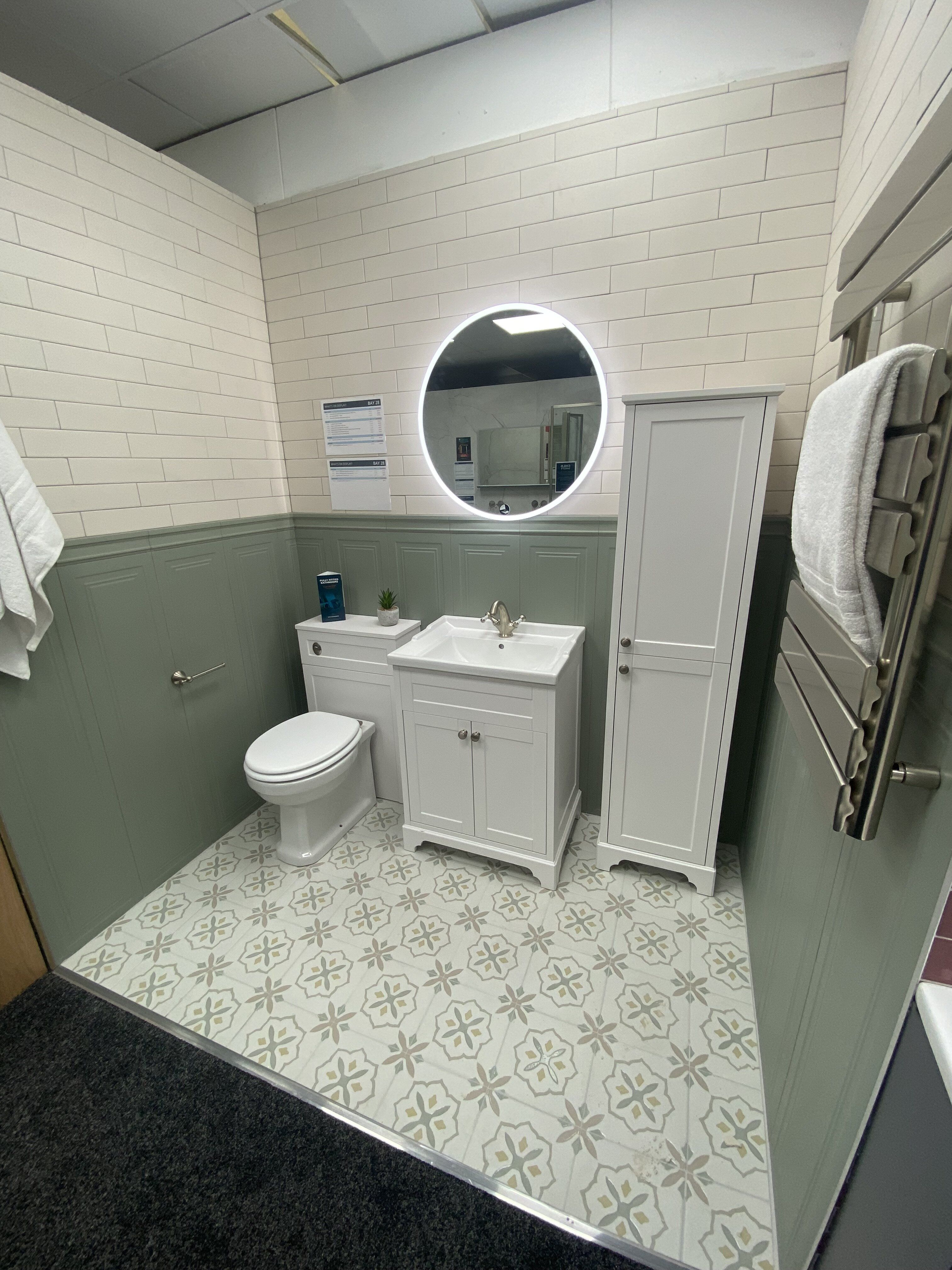 Green and white bathroom display at Easy Bathrooms Newbury with vanity furniture, toilet and illuminated mirror.