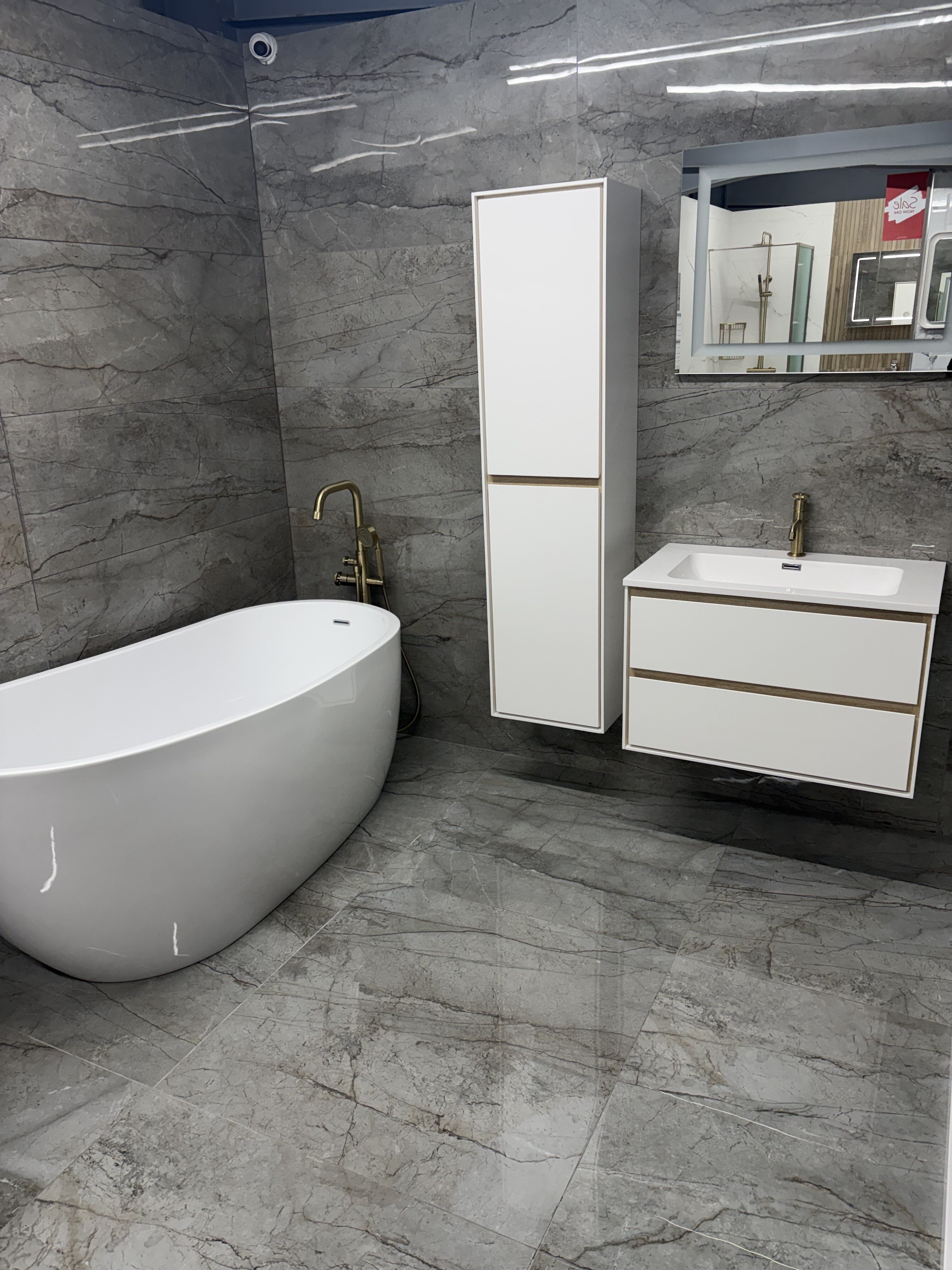 Luxury bathroom display at Easy Bathrooms Basildon featuring a white freestanding bath, wall-hung furniture and brushed gold fittings.