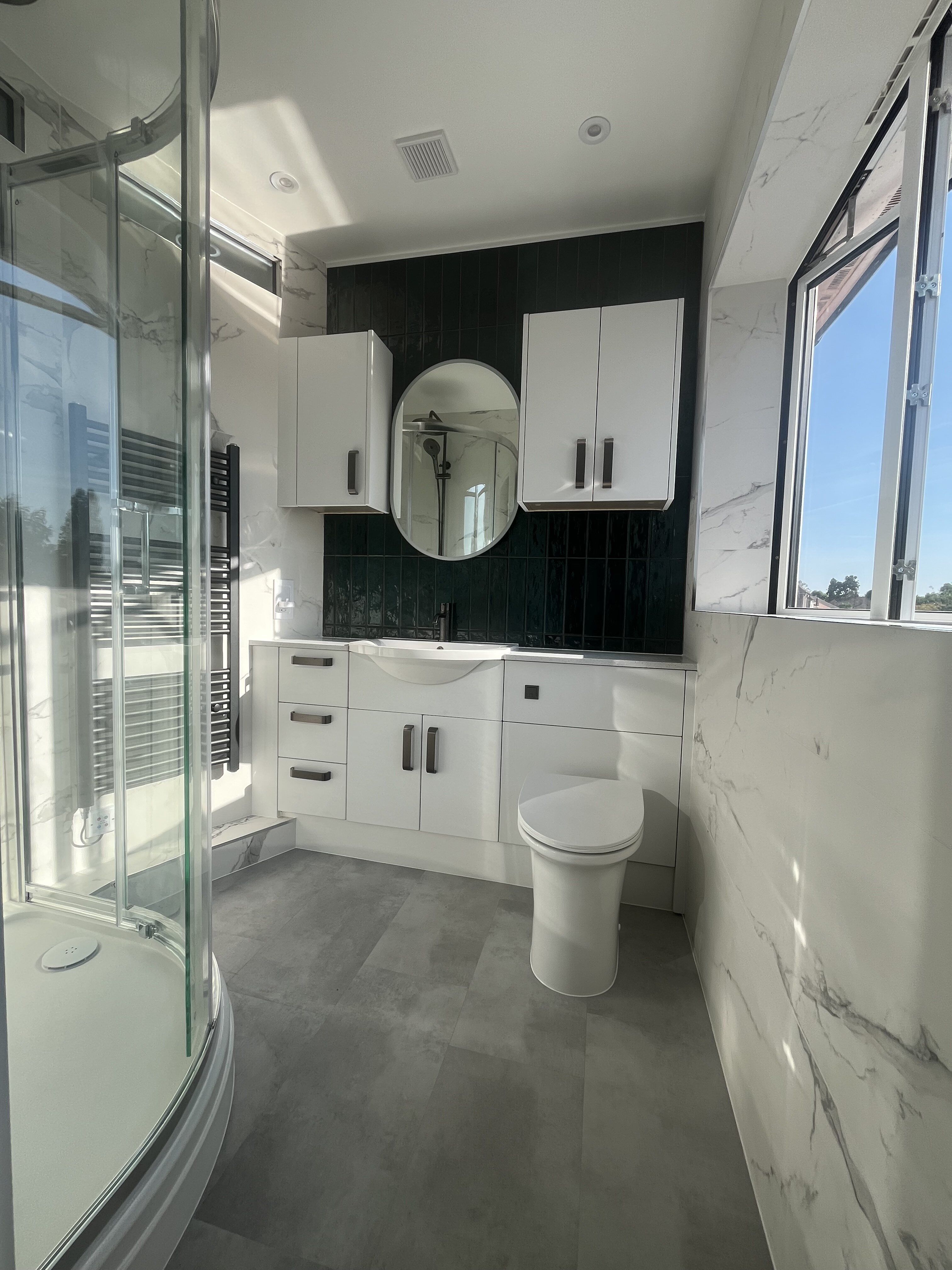 Finished Chichester customer bathroom featuring marble-effect tiles, curved shower enclosure and black brassware.