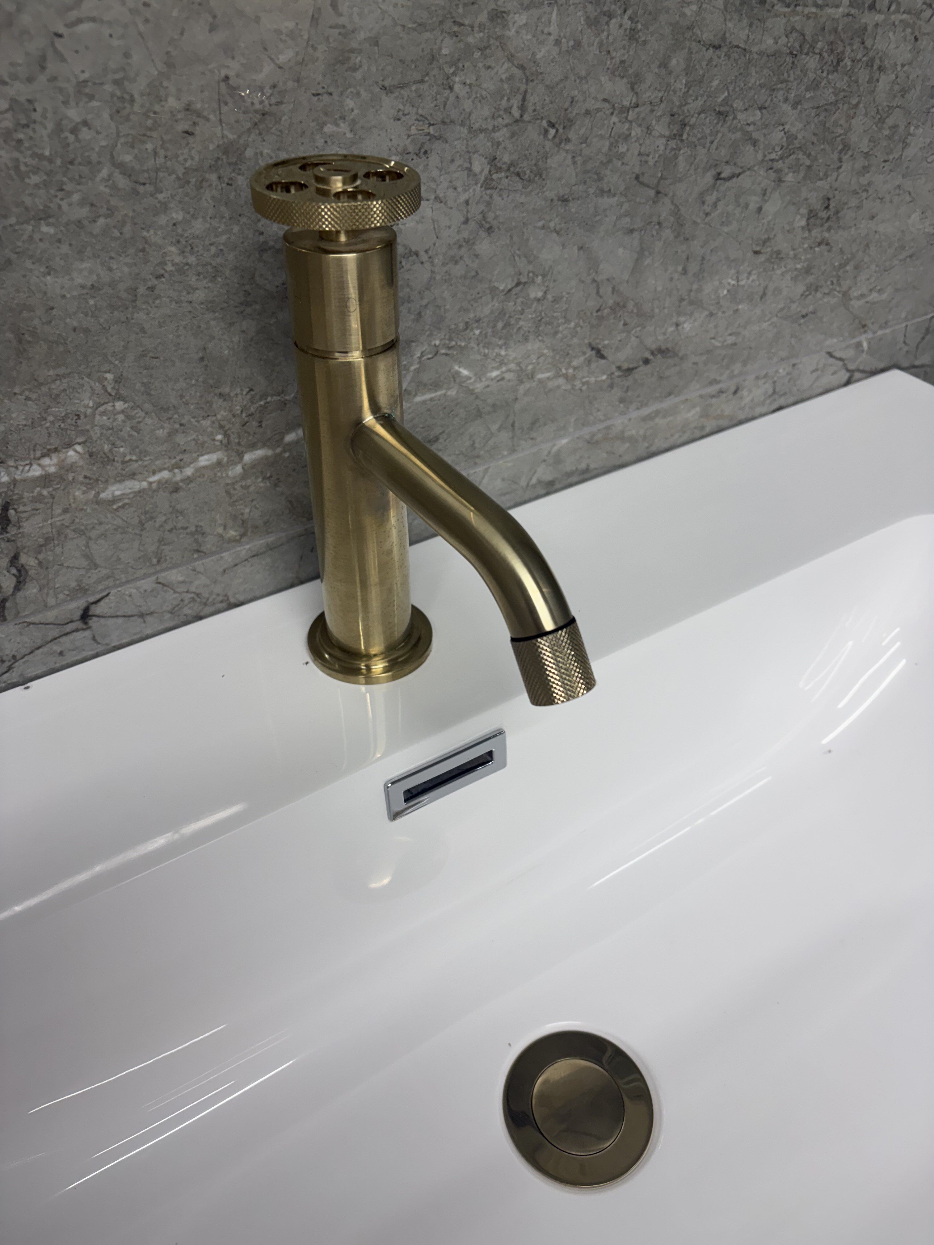 Close-up of a brushed gold basin tap and waste on a white basin at Easy Bathrooms Basildon.