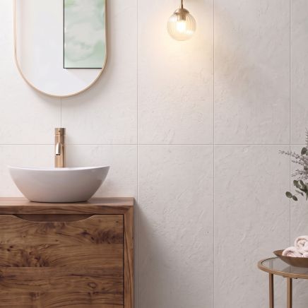 Modern bathroom wall vertically tiled in Kenya Blanco Ceramic Wall Tiles behind a wooden vanity with brass mixer.