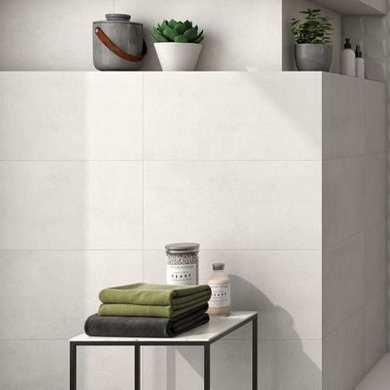 Modern bathroom corner tiled in Kenya Blanco Rectified Ceramic Wall Tiles with folded green towels on a table.