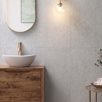 Modern bathroom wall vertically tiled in Kenya Gris Ceramic Wall Tiles behind a wooden vanity with brass mixer.