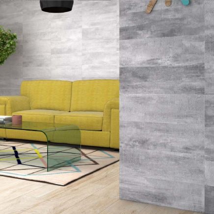 Living room partition wall tiled in Keywood Gris Ceramic Tiles beside a yellow sofa and glass coffee table.