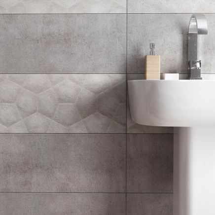 Modern bathroom wall tiled in Moonlight Ceniza Ceramic Tiles with a middle band of Arkan 3D geometric feature tiles behind a white pedestal basin