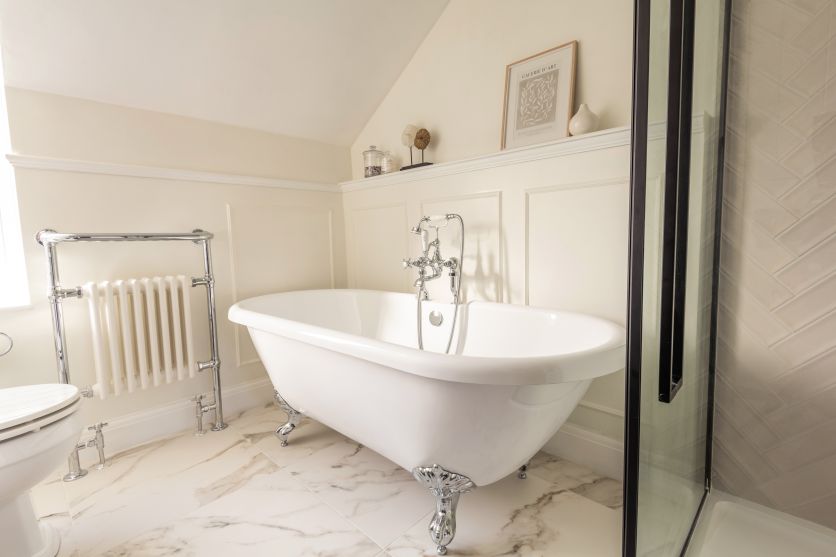 Traditional bathroom with white clawfoot bath, marble floor tiles, chrome towel rail and classic panelled walls.