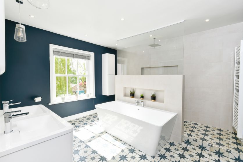 Modern bathroom with navy walls, star-pattern floor tiles, white freestanding bath and chrome fixtures.