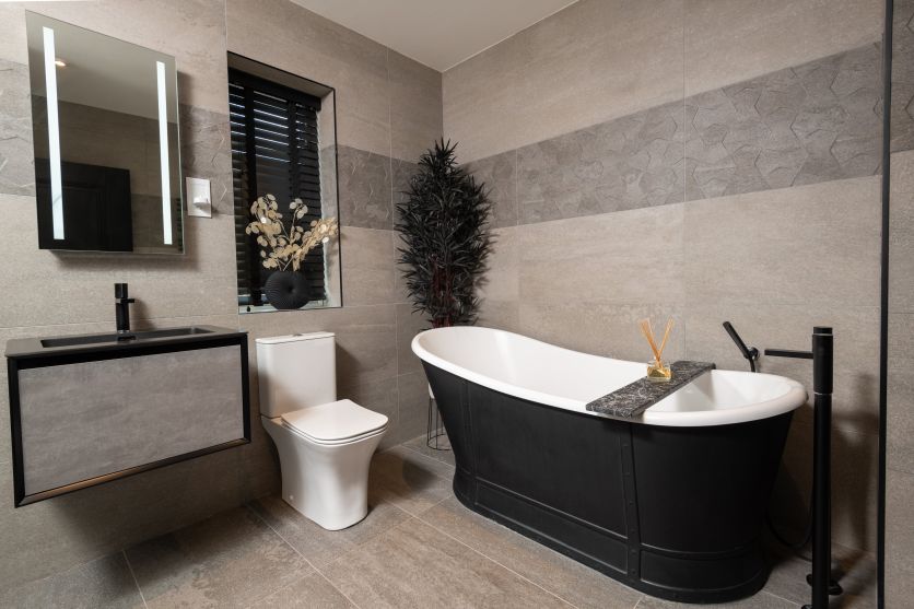 Modern black and grey bathroom with freestanding black bath, textured grey tiles, wall-hung vanity and LED mirror.
