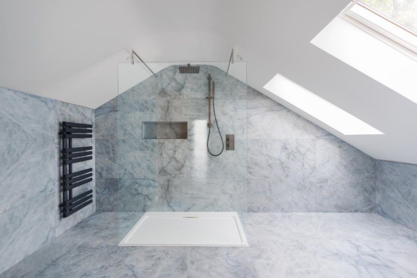 A spacious wetroom under a sloping ceiling, featuring Kendrick Sky blue marble-effect porcelain tiles, an Oxford walk-in shower screen, and Zena gunmetal shower fittings.