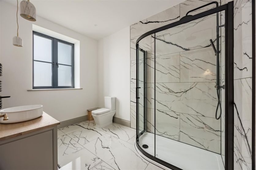 A bright, modern bathroom featuring Marquis White Marble gloss porcelain tiles on the walls and floor, accented by a Fabio black sliding quadrant shower door and a matching Elora matt black thermostatic shower set.