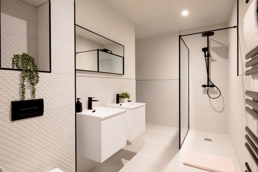 A modern neutral wetroom featuring an Amien matt black framed fluted glass shower screen and Camden dual shower pack, complemented by Chester Beige decor tiles and a Kendal matt white wall-hung vanity unit.