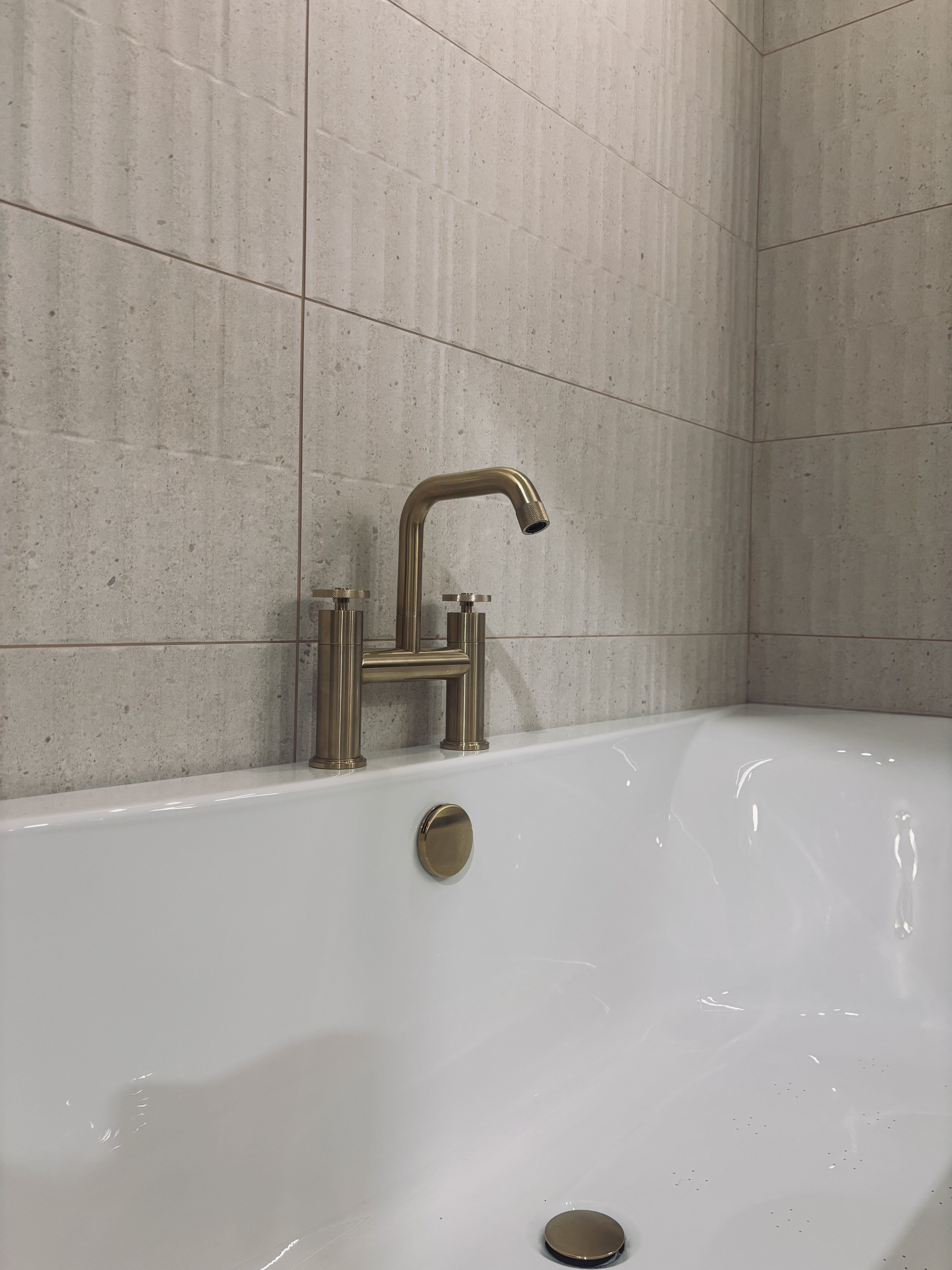 Brushed gold brassware bath filler tap and ribbed natural stone effect tiles
