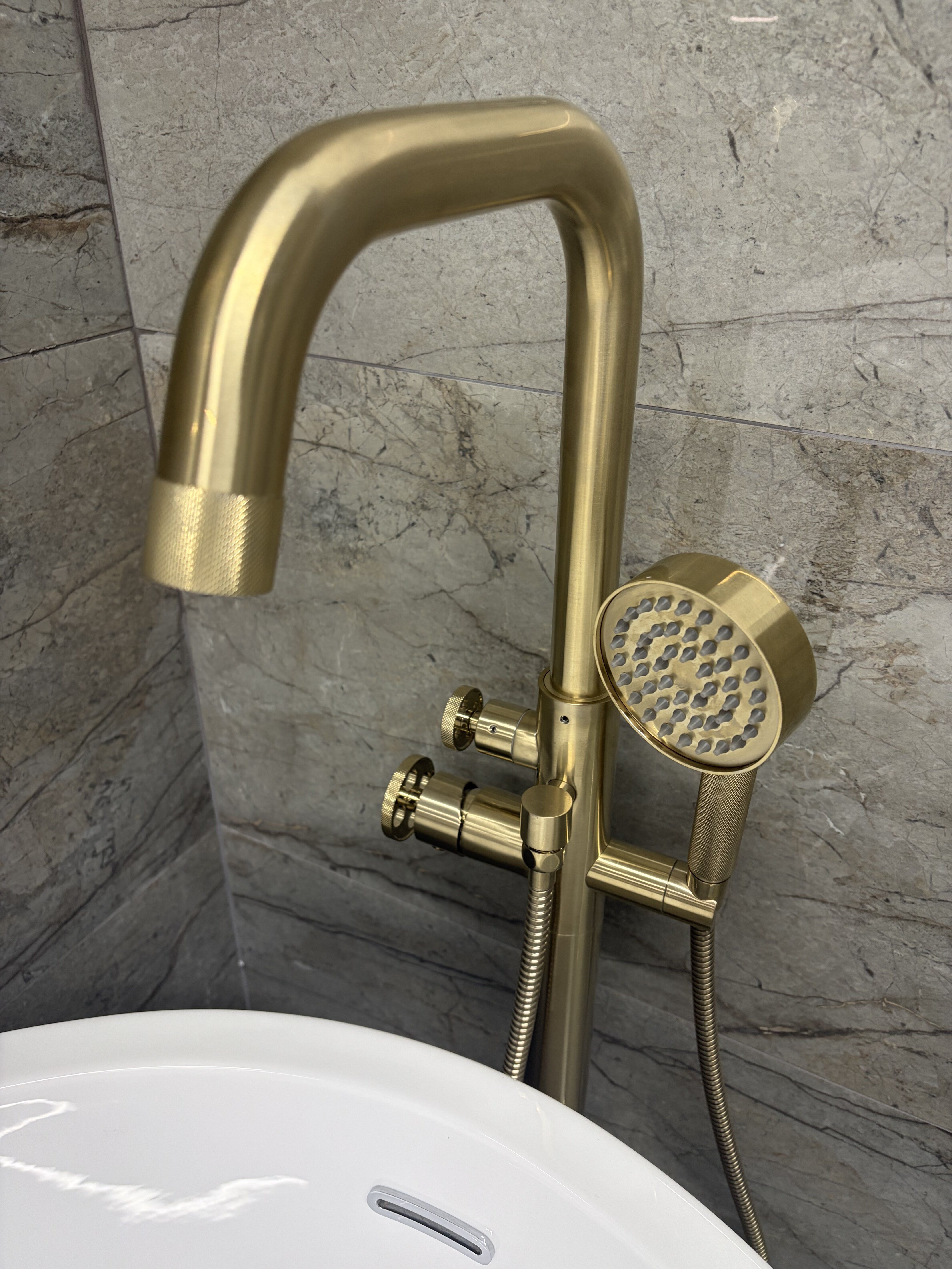 Brushed gold basin tap on display at Easy Bathrooms Basildon with neutral stone-effect tiles.