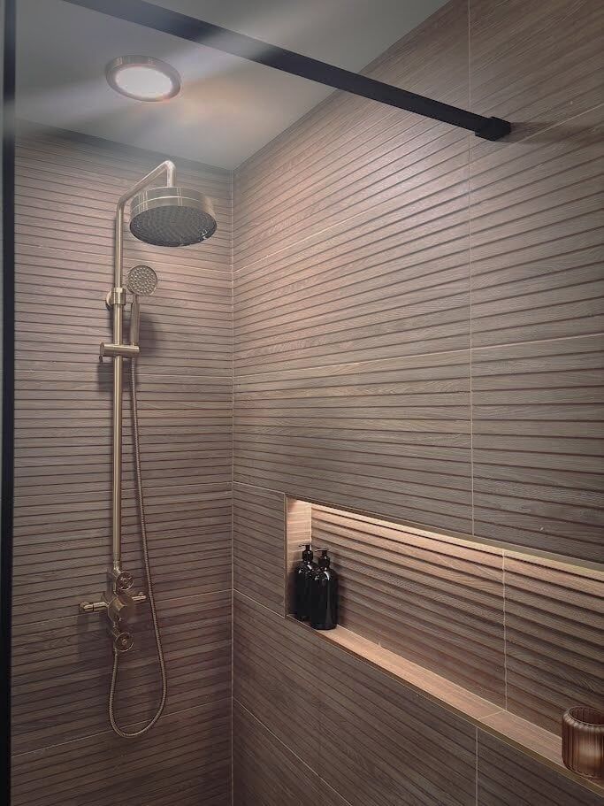 Brushed gold shower and frameless shower screen in a walk in shower area with niche and accent lighting