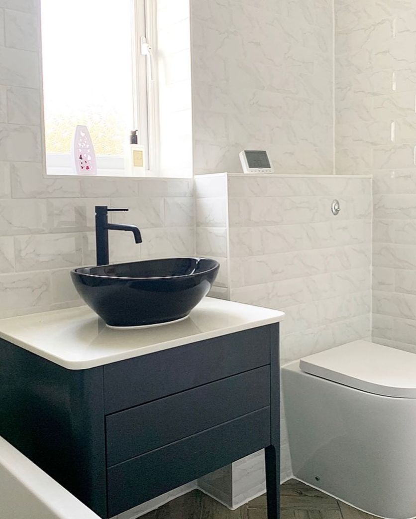 A contemporary black countertop basin with a matte black mixer tap, situated on a navy blue vanity unit against marble-effect metro wall tiles.