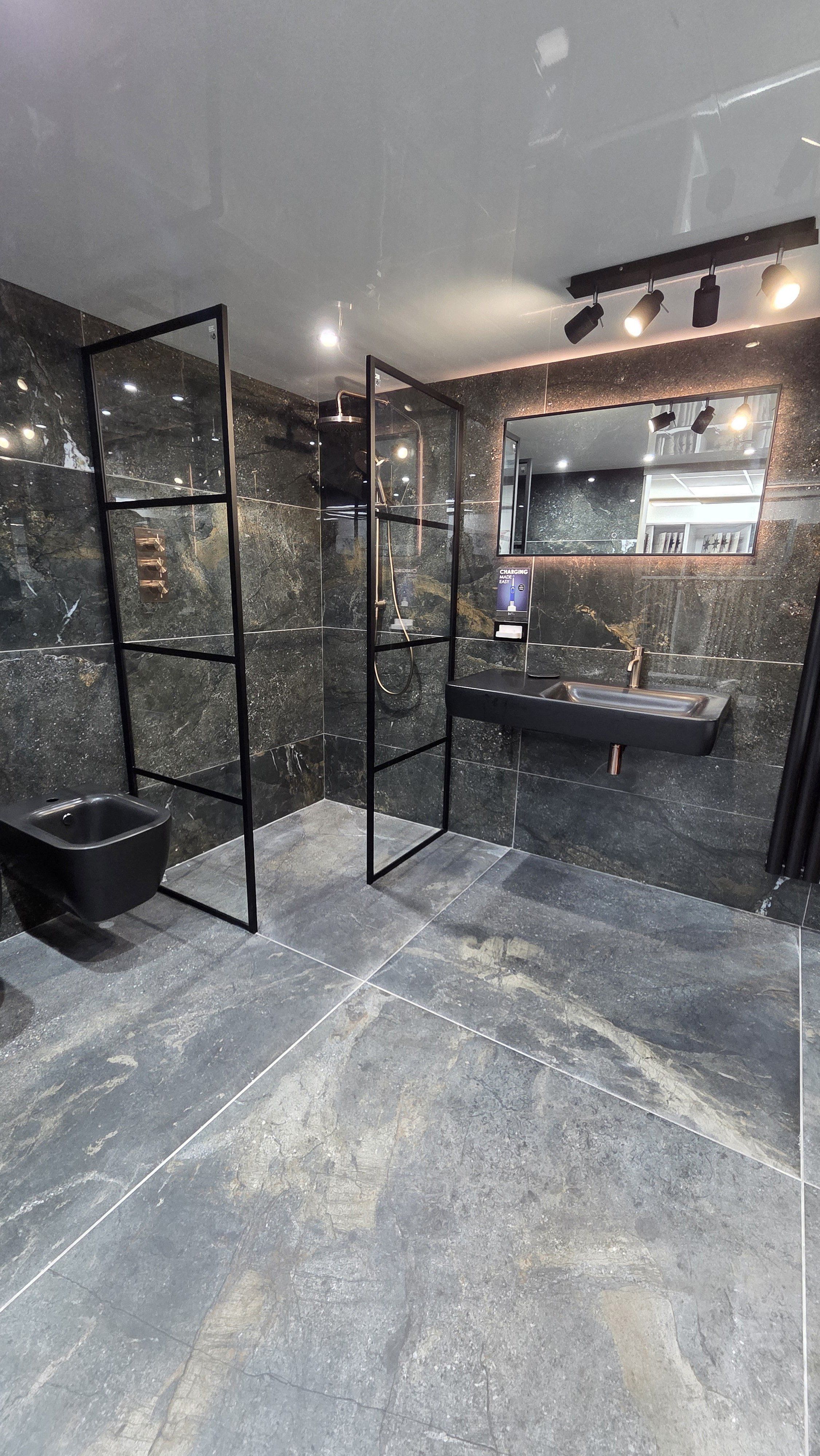 Dark marble-effect bathroom display at the Easy Bathrooms Sittingbourne showroom, featuring a black framed walk-in shower, wall-hung toilet, black basin and illuminated mirror