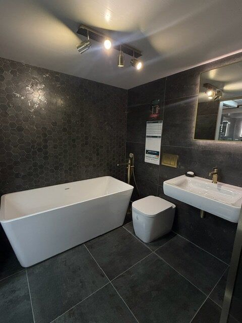 Freestanding white bath displayed against deep charcoal tiles in the Easy Bathrooms High Wycombe showroom.