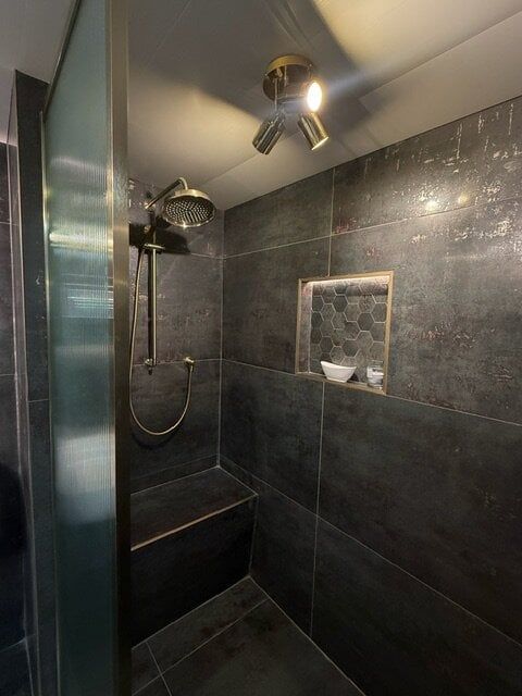 Walk-in shower with dark tiles, brushed brass rainfall shower and built-in tiled seating area.